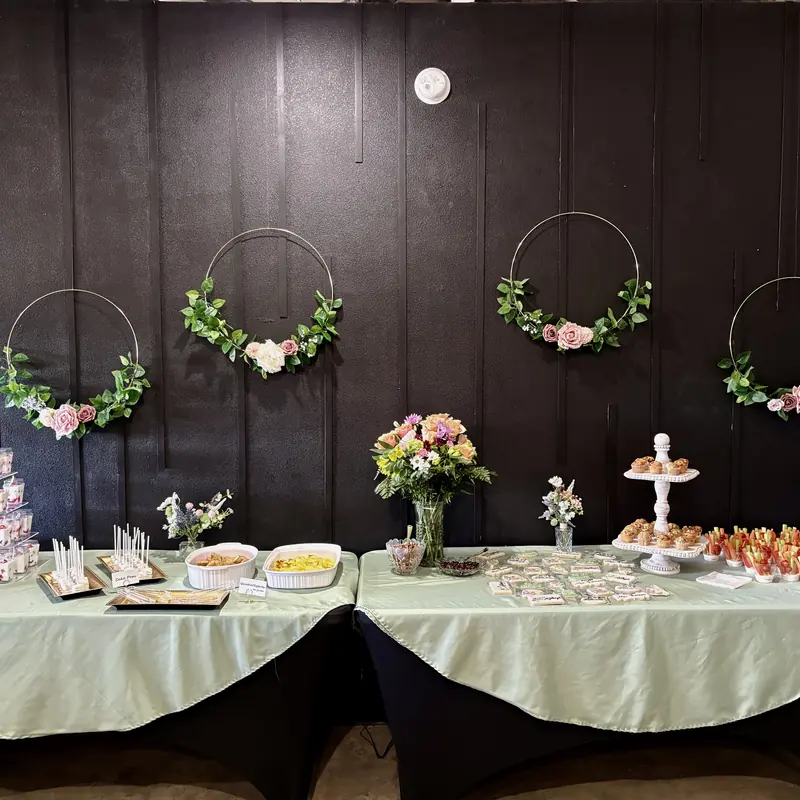 A dessert table on sage linen under floral hoops on the black wall