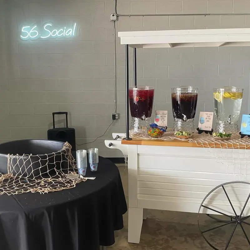 Drink dispensers on the bar cart under the 56 Social neon sign