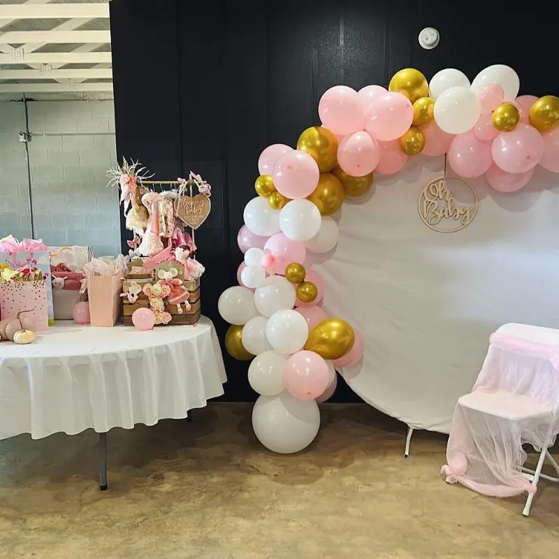 A pink and gold balloon arch beside a dessert table